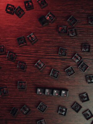 Scattered keyboard keys spelling 'SCAM' on a red-lit wooden surface, symbolizing online fraud.